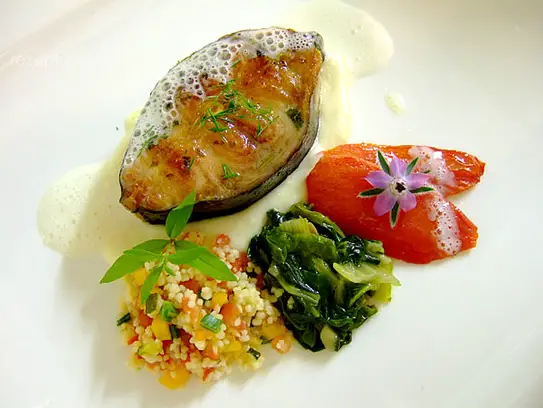 Gebratene Wallerschnitte auf Gemüsekuskus, sautierten Spinat und Tomatenfilets