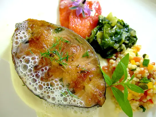 Gebratene Wallerschnitte auf Gemüsekuskus, sautierten Spinat und Tomatenfilets