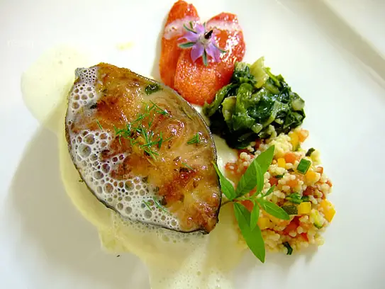 Gebratene Wallerschnitte auf Gemüsekuskus, sautierten Spinat und Tomatenfilets